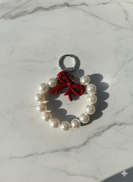 Pearl ring bag charm with glossy red enamel bow on marble surface