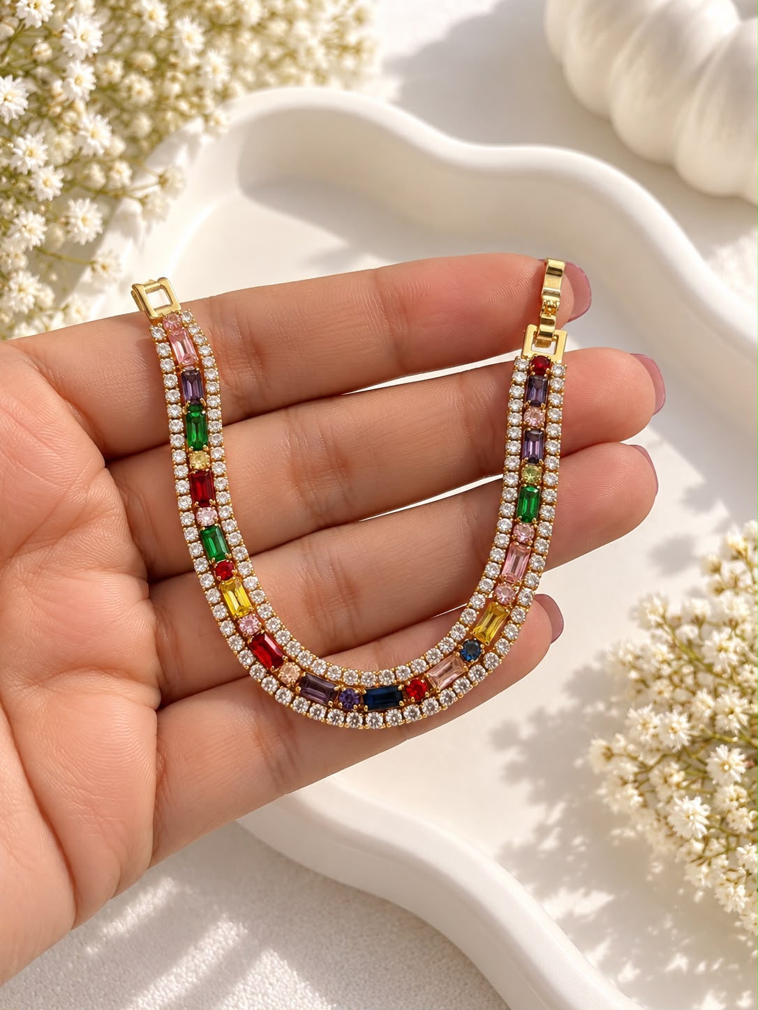Multicolour rectangular stone bracelet held in a hand showing its gold-tone clasp