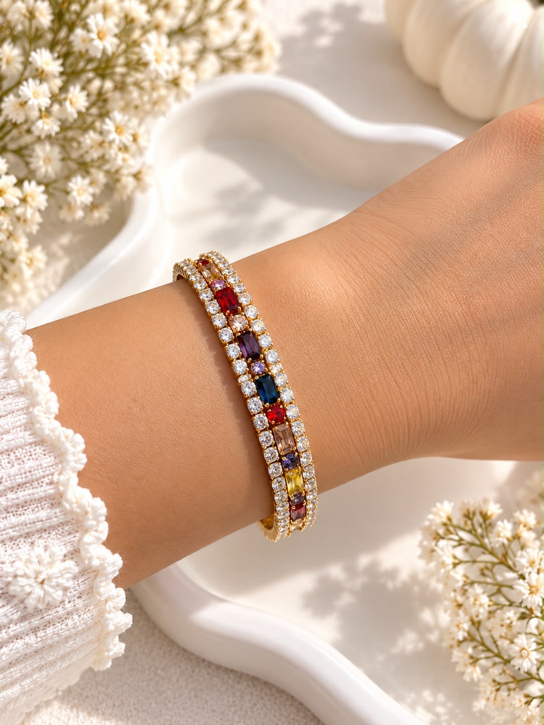 Gold-tone multicolour stone bracelet with clear stone borders worn on a wrist