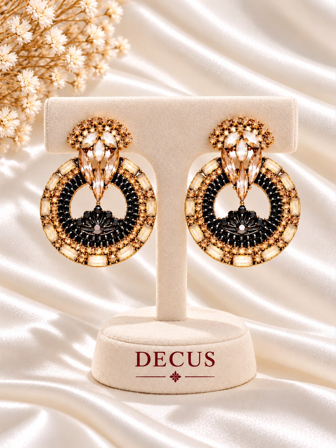 Black-and-gold circular statement earrings with clear stone accents on a Decus display stand