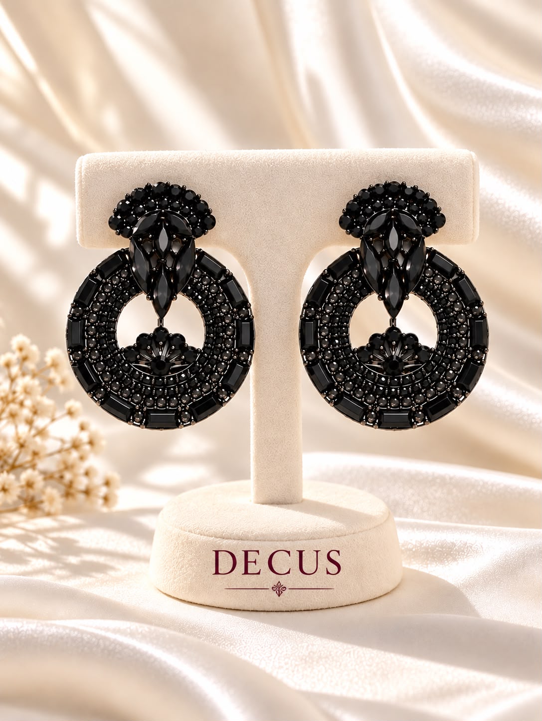 Black circular statement earrings with dark stone detailing on a Decus display stand
