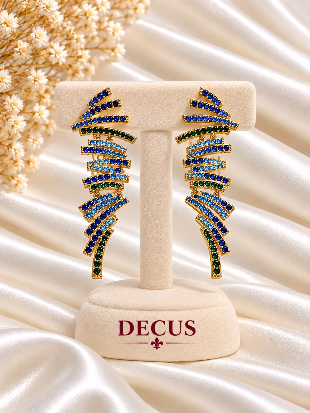 Blue and green stone cascade statement earrings in a gold-tone setting on a Decus display stand