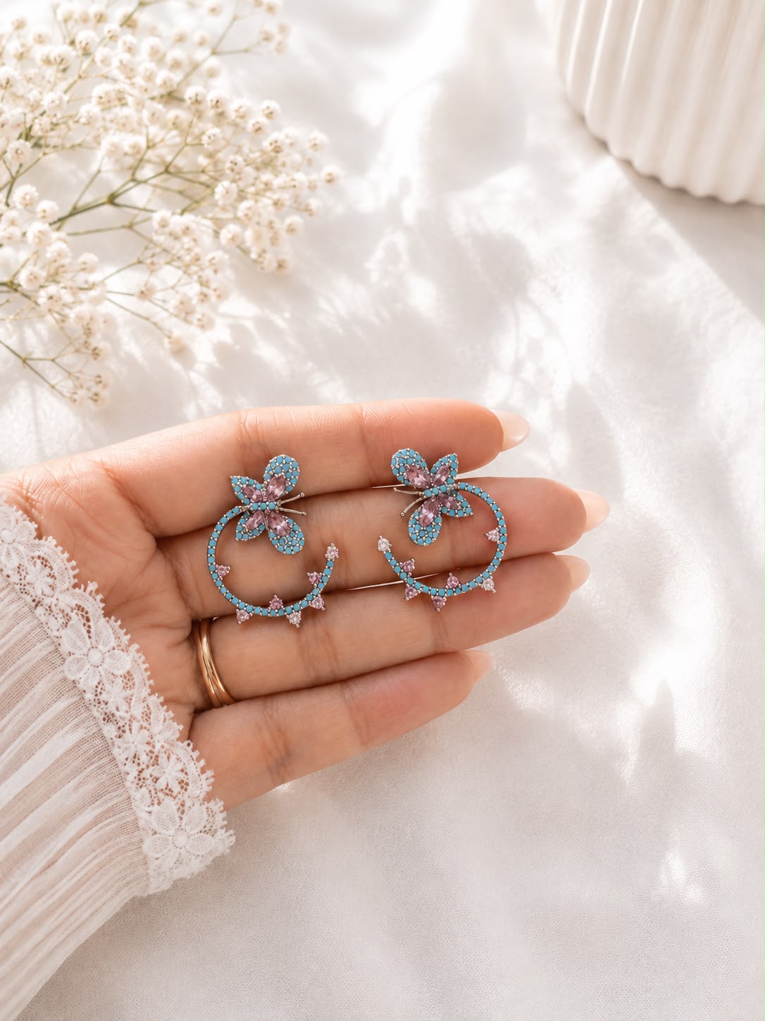 Turquoise butterfly hoop earrings held in hand to show scale