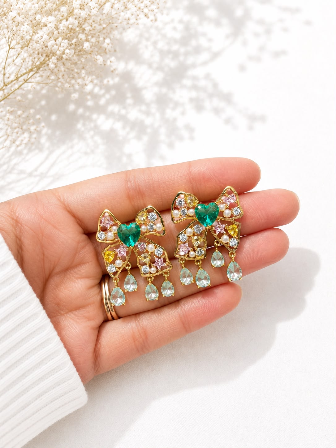 Emerald heart bow drop earrings held in hand to show scale